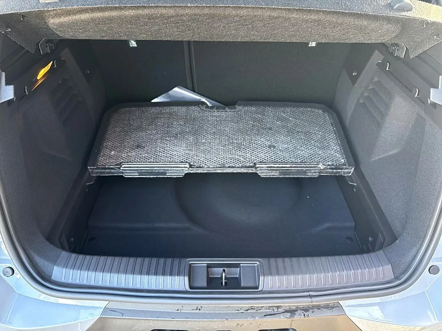 Coffre ouvert d’une Renault Symbioz gris rafale, montrant le plancher de coffre mobile et l’espace de rangement.