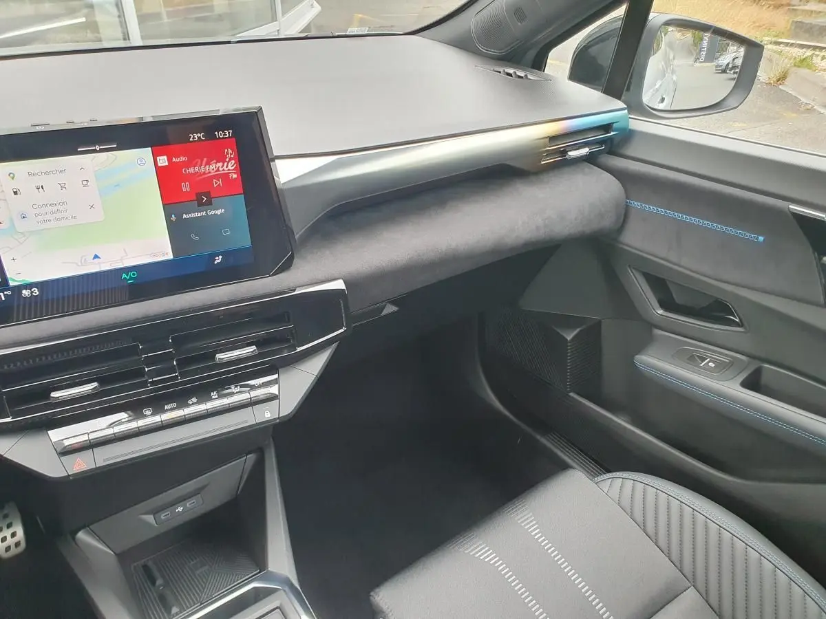 Vue intérieure côté passager de la Renault Clio VI hybride 2026, tableau de bord moderne avec écran tactile et surpiqûres bleues.