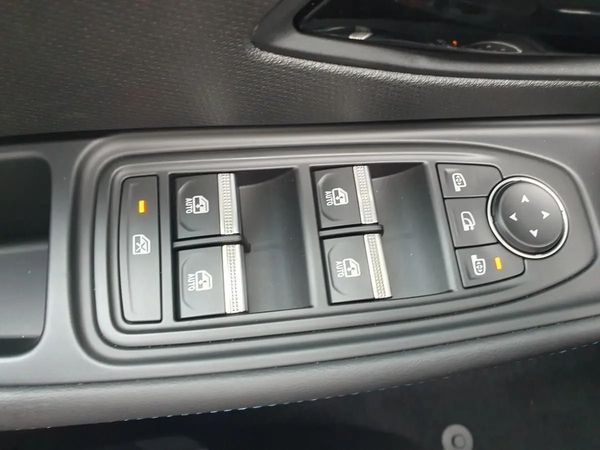 Gros plan sur les commandes de lève-vitres et réglage des rétroviseurs côté conducteur de la Renault Clio VI gris Rafale.