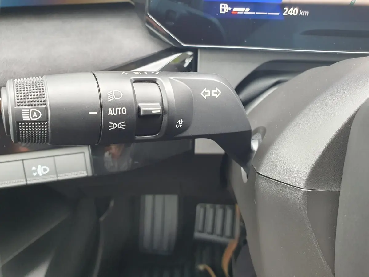 Gros plan sur la commande des feux et clignotants côté gauche du volant d’une Renault Clio VI gris Rafale, tableau de bord partiellement visible.