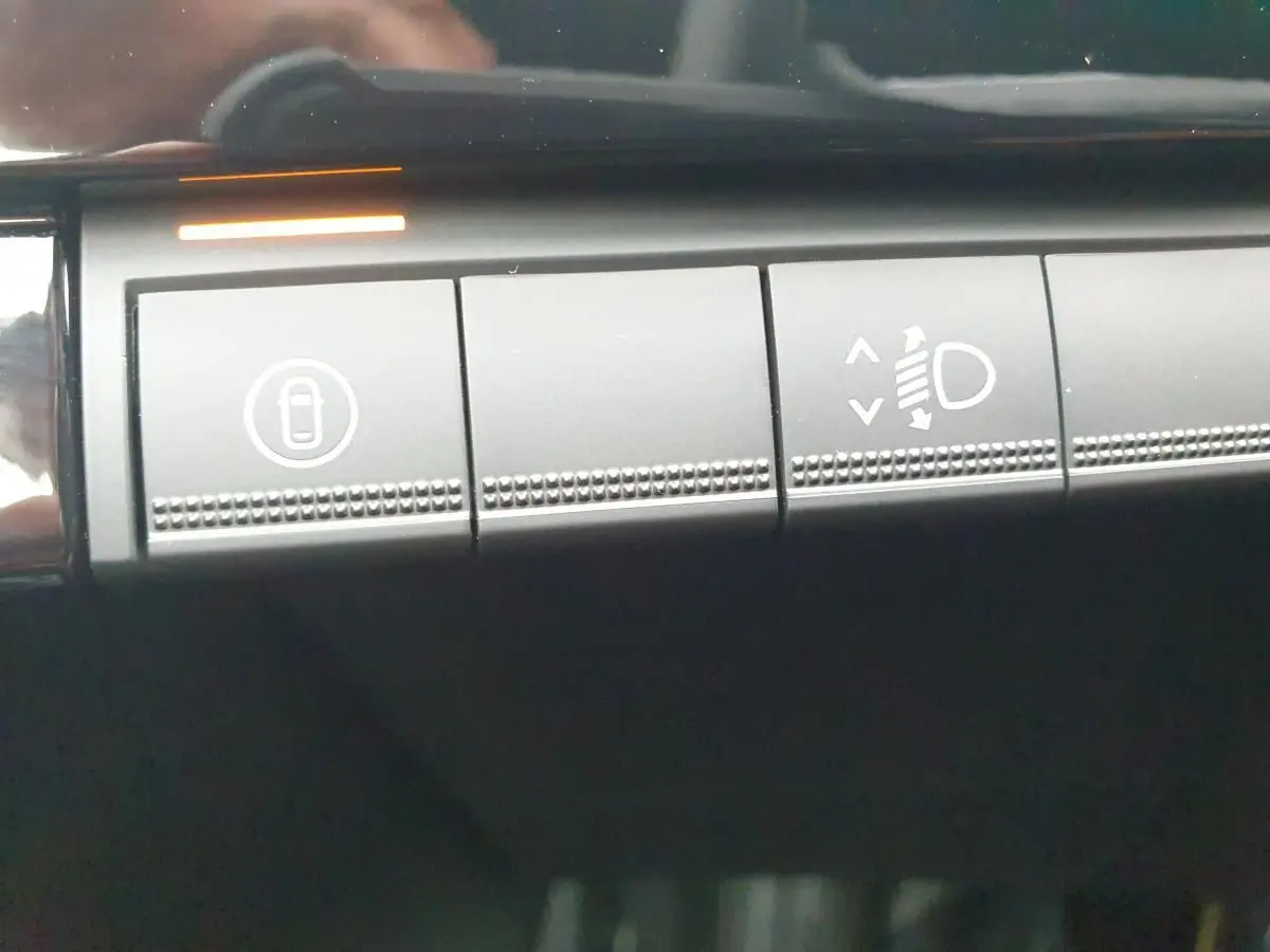 Gros plan sur les boutons de commande intérieurs gris foncé de la Renault Clio VI, avec éclairage orange actif.