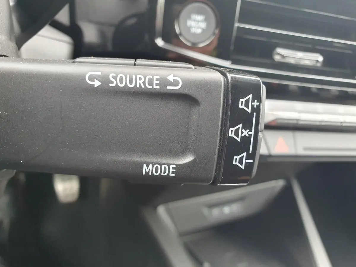Gros plan sur la commande audio au volant de la Renault Clio VI gris Rafale, avec tableau de bord en arrière-plan flou.