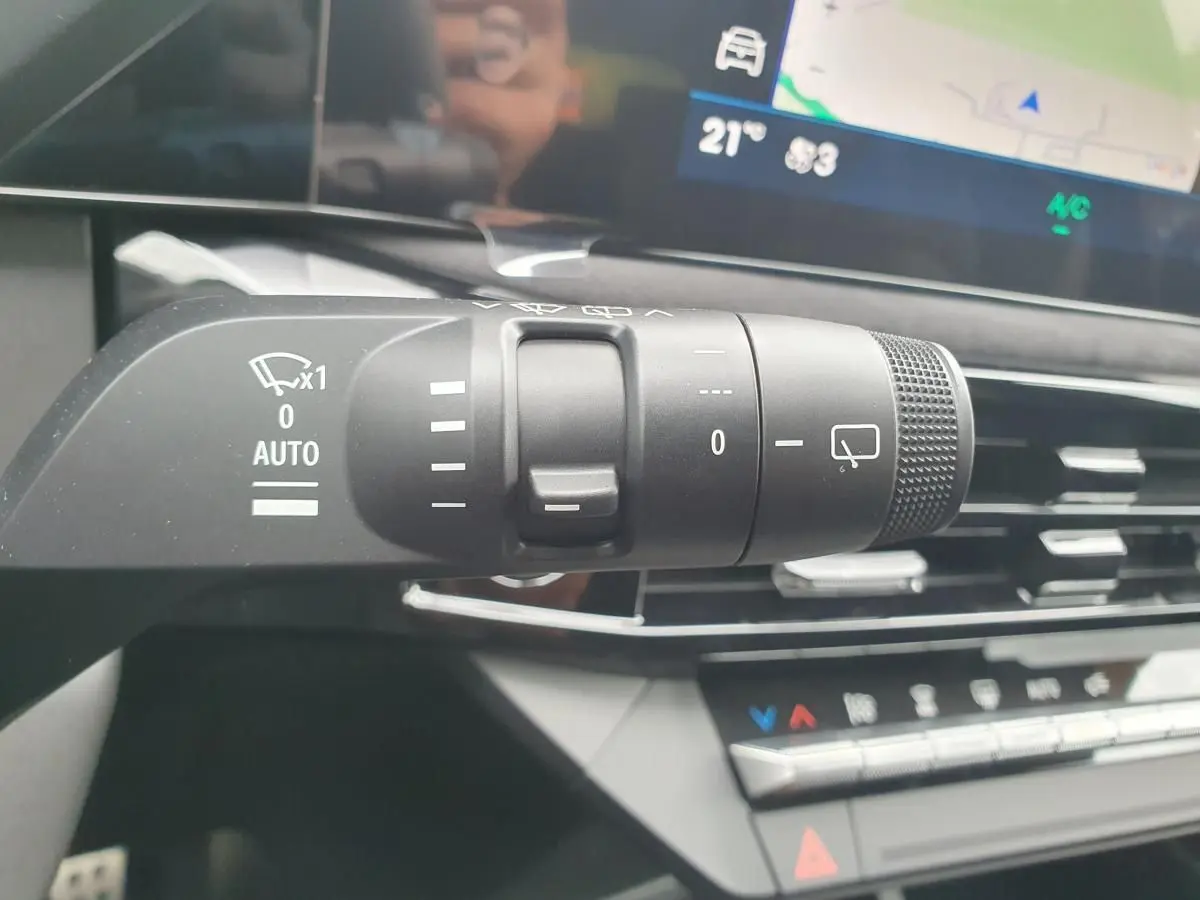 Gros plan sur la commande des essuie-glaces dans l’habitacle de la Renault Clio VI gris Rafale, avec écran tactile en arrière-plan.