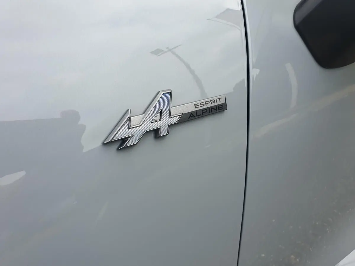 Gros plan sur l'écusson Esprit Alpine argenté sur la porte gris rafale d'une Renault Clio VI hybride.