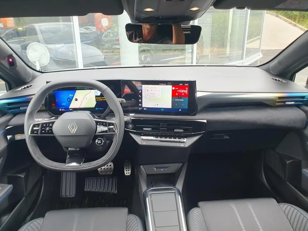 Vue intérieure avant de la Renault Clio VI hybride, tableau de bord moderne avec écran tactile large et volant multifonction.