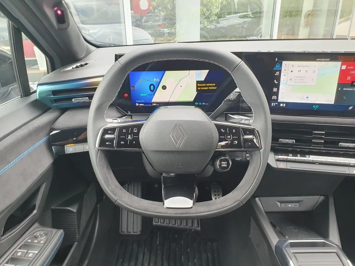 Vue frontale de l’habitacle de la Renault Clio VI hybride, volant multifonction et tableau de bord numérique.