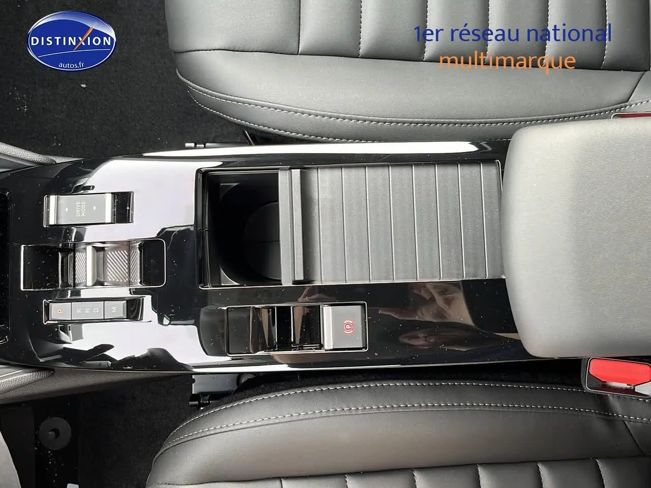 Vue plongeante sur la console centrale noire brillante du Citroën C4 1.2 hybride 2025 avec accoudoir et sièges cuir gris.