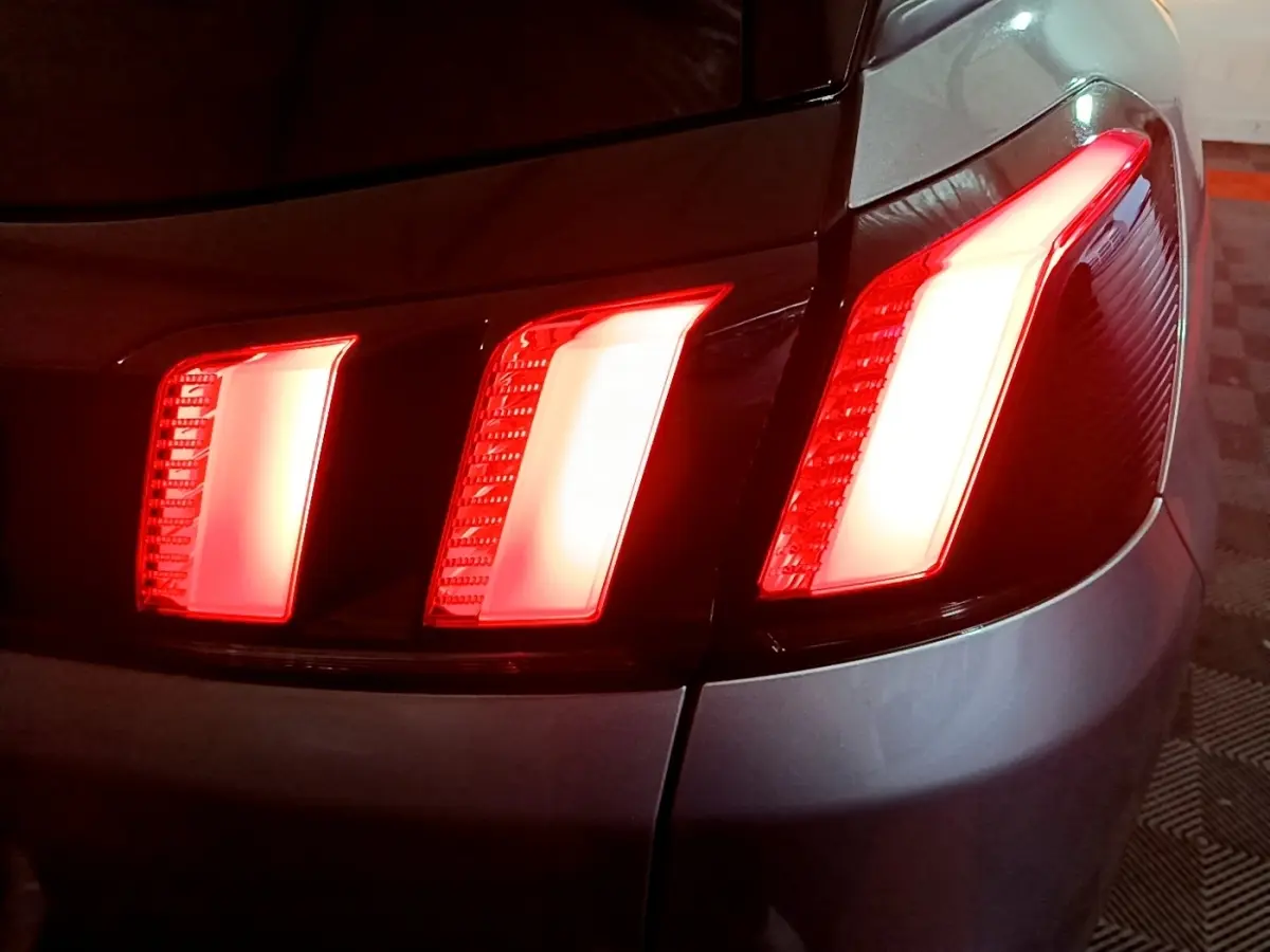 Gros plan sur les feux arrière allumés côté gauche d’un Peugeot 3008 gris clair, version 2020.