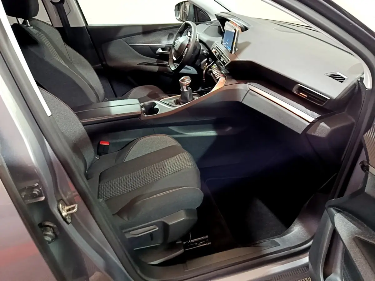 Vue intérieure côté conducteur du Peugeot 3008 gris clair, mettant en valeur le tableau de bord moderne avec écran tactile et volant cuir.