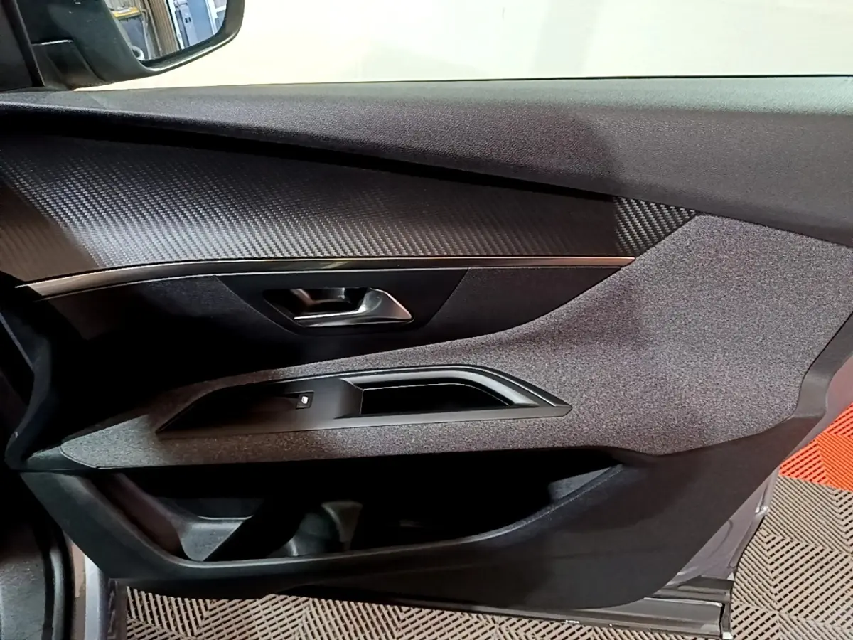 Vue intérieure du panneau de porte côté conducteur de la Peugeot 3008 gris clair, avec finition tissu et insert imitation carbone.