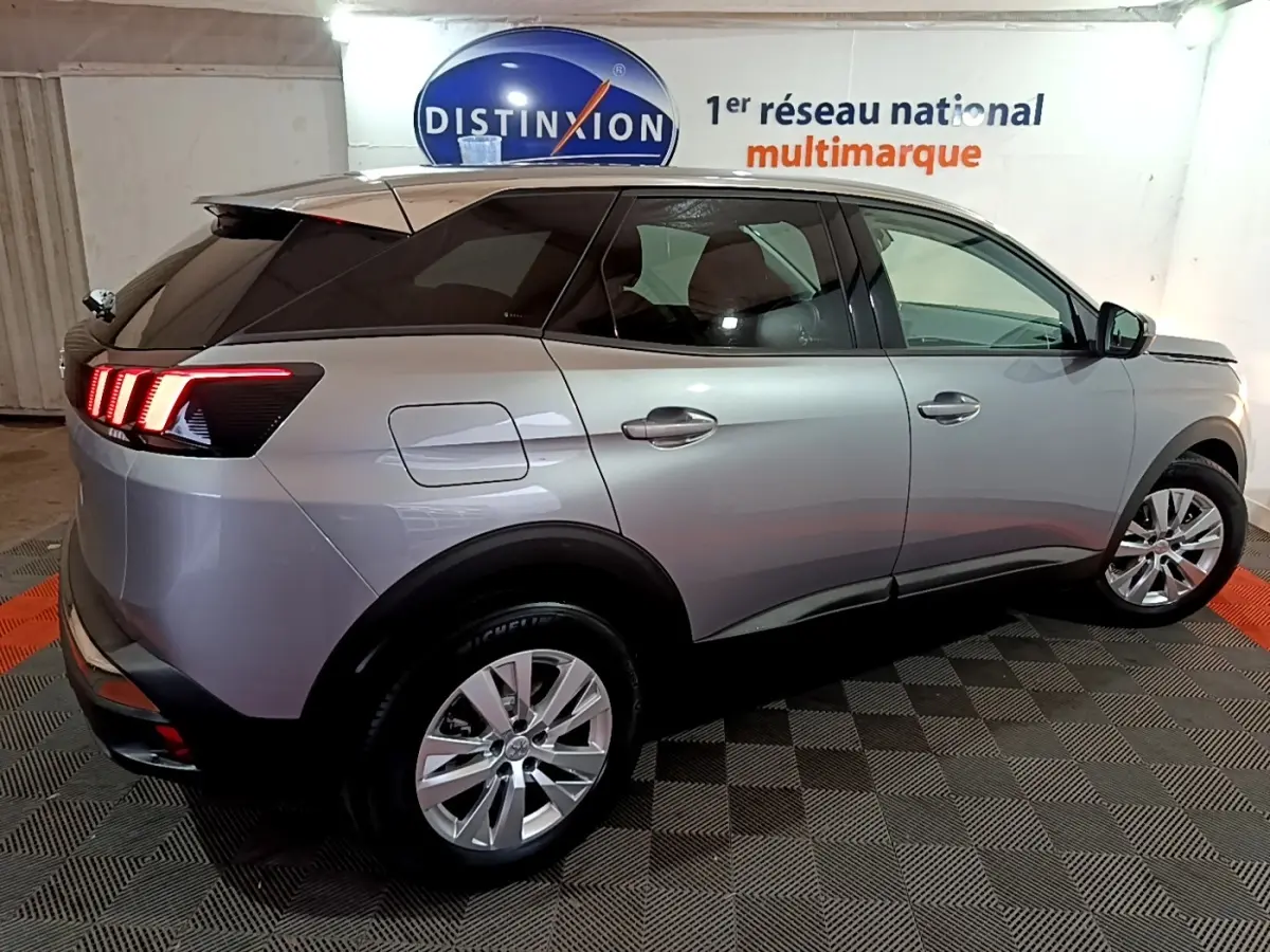 Vue 3/4 arrière droite d’un Peugeot 3008 gris clair avec feux LED distinctifs et jantes alliage en intérieur showroom.