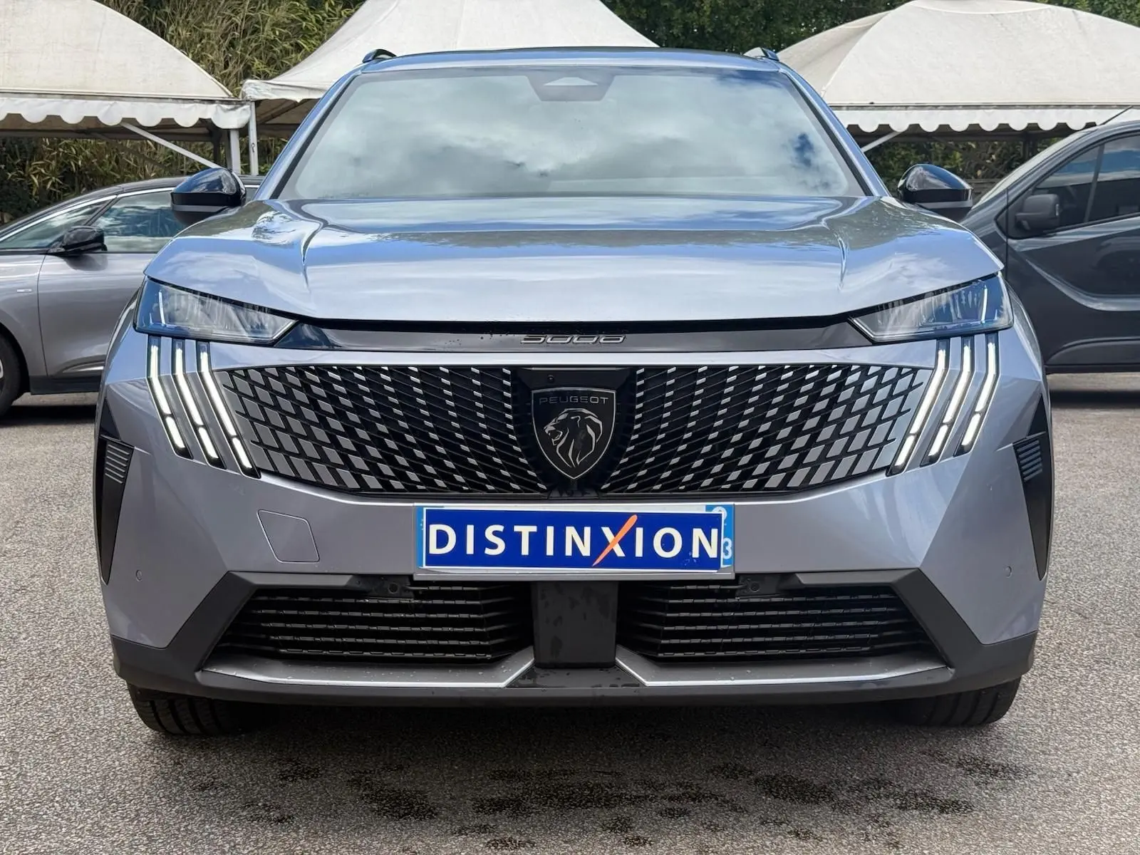 Vue frontale d'un Peugeot 5008 gris Artense 2025 avec calandre noire à motif géométrique et feux LED verticaux distinctifs.