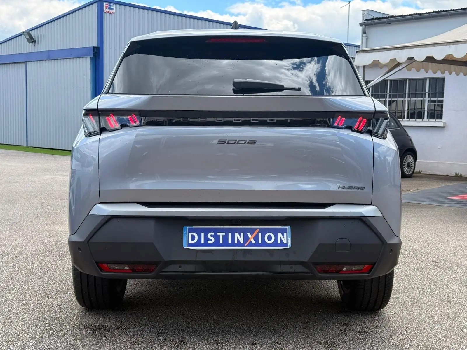 Vue arrière d'un Peugeot 5008 gris Artense hybride 2025 avec feux arrière LED distinctifs et plaque d'immatriculation Distinxion.