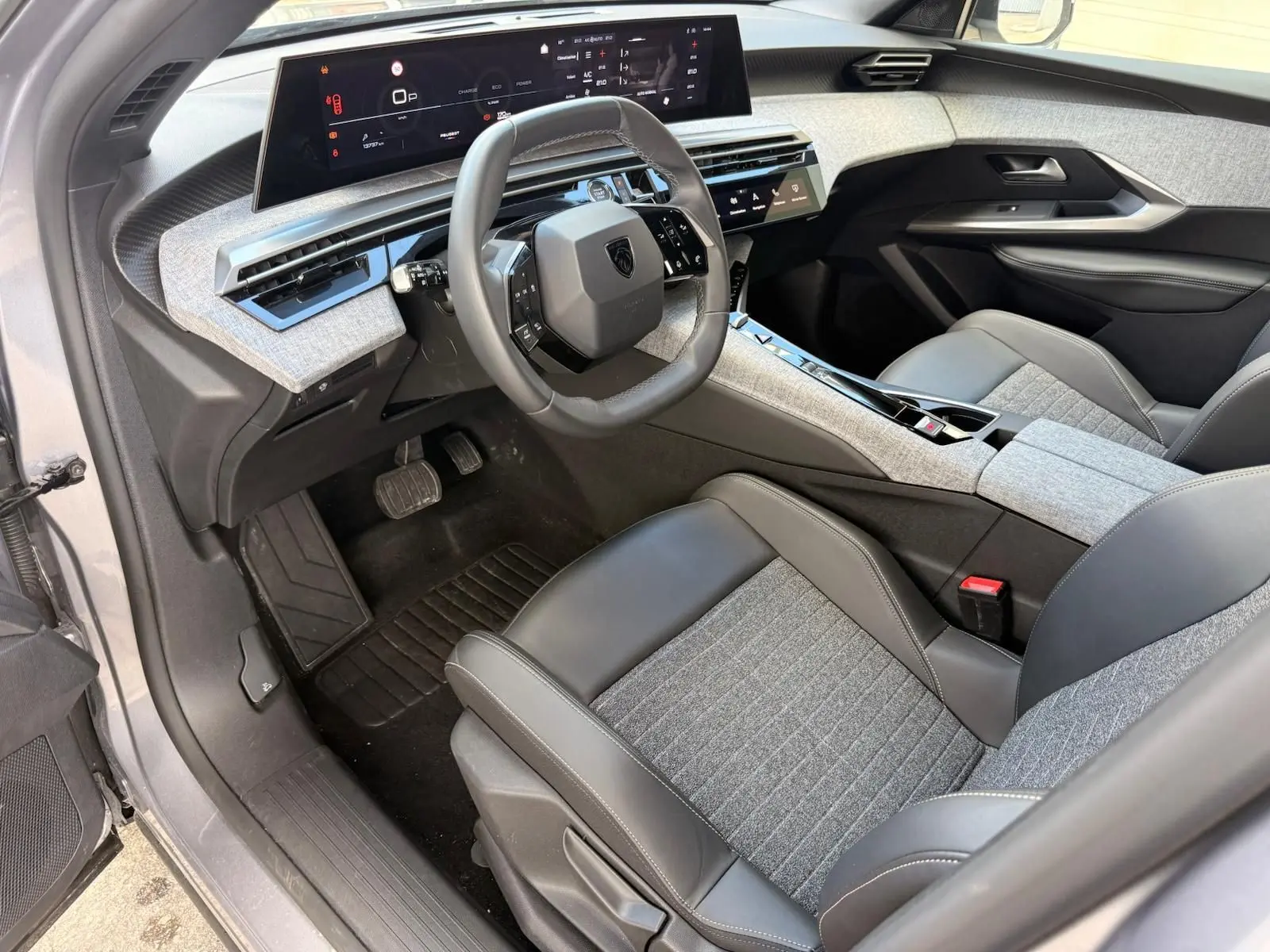 Vue intérieure côté conducteur du Peugeot 5008 Hybrid 145 en gris Artense, avec tableau de bord numérique et sellerie mixte tissu-cuir gris.