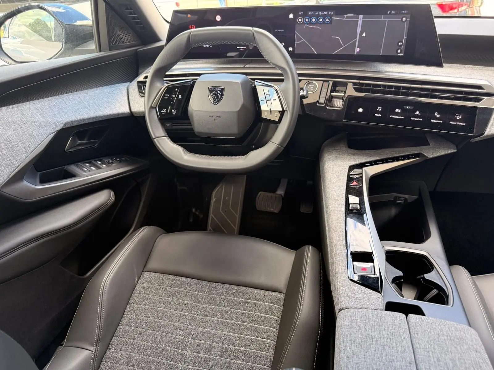 Vue intérieure avant du Peugeot 5008 Hybrid 145 en gris avec volant compact, tableau de bord numérique et console centrale en tissu gris.