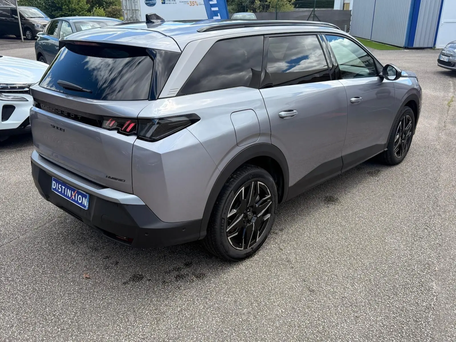 Vue 3/4 arrière droite du Peugeot 5008 Hybrid gris Artense avec vitres teintées et jantes noires distinctives.