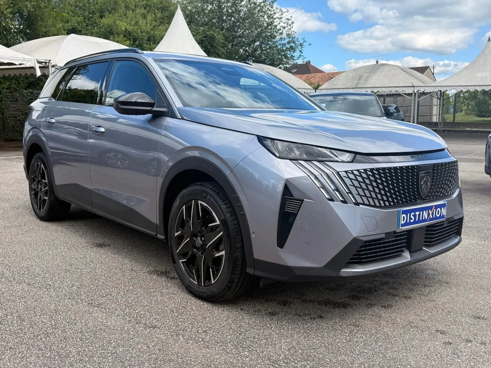 Peugeot 5008 Hybrid gris Artense en 3/4 avant droit, avec calandre noire et jantes alliage noires distinctives.
