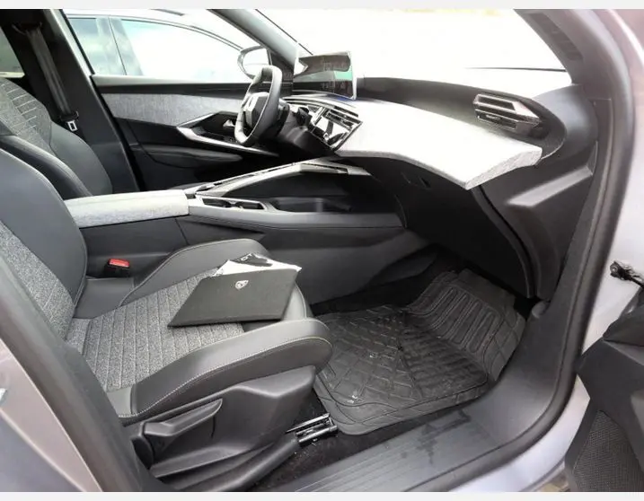 Vue intérieure côté passager du Peugeot 5008 Hybrid 2025 gris Artense, avec tableau de bord moderne et sièges tissu gris.