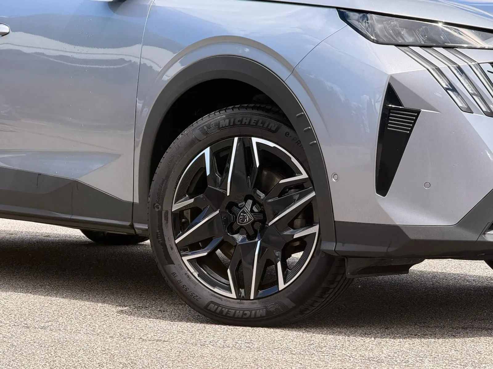 Gros plan sur la roue avant droite et partie avant d’un Peugeot 5008 gris Artense avec jante noire et argentée.