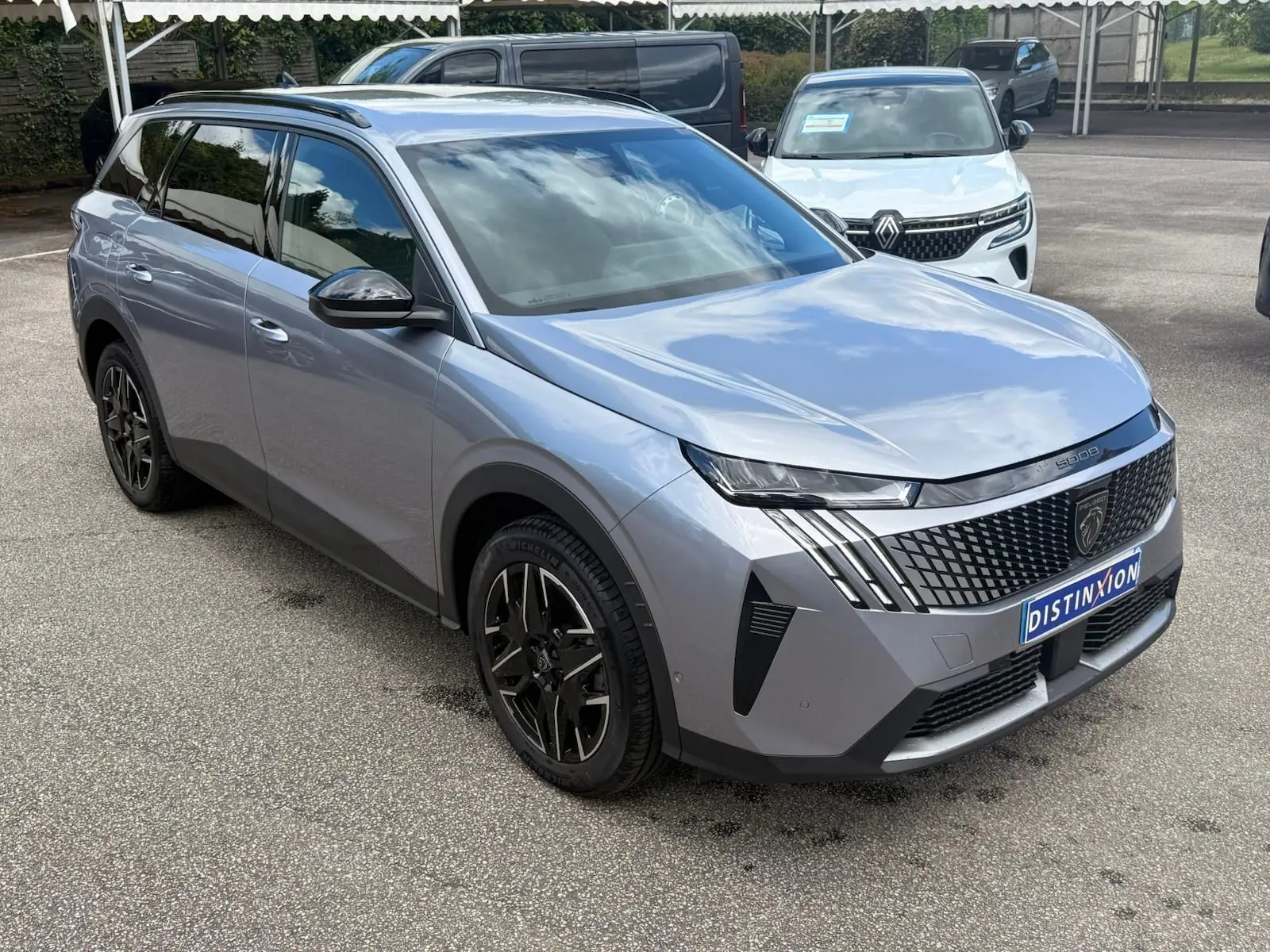 Peugeot 5008 Hybrid gris Artense en 3/4 avant droit, avec calandre distinctive et jantes noires stylées.