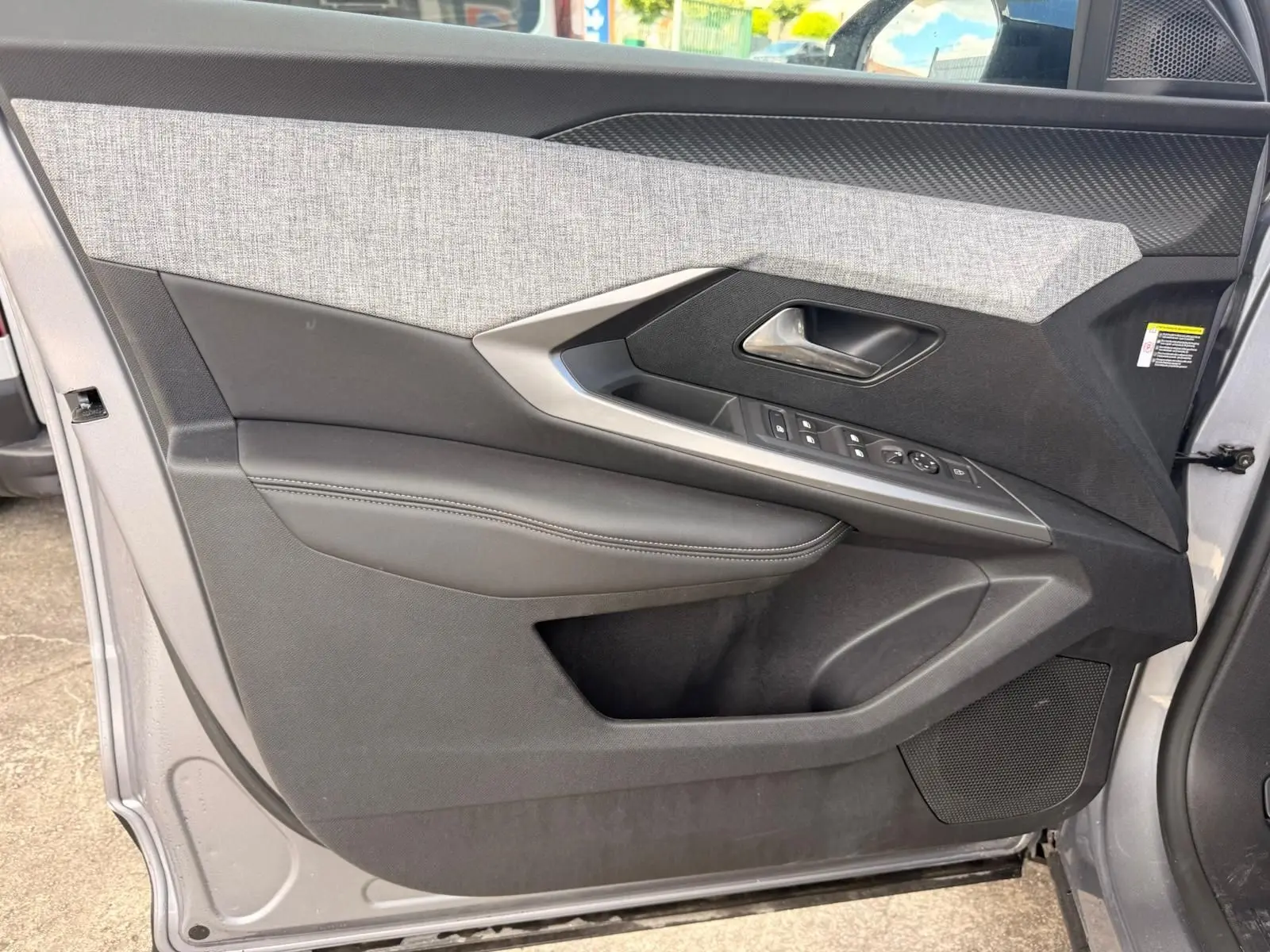 Vue intérieure côté gauche de la porte avant d’un Peugeot 5008 gris Artense, avec garniture tissu et commandes électriques.