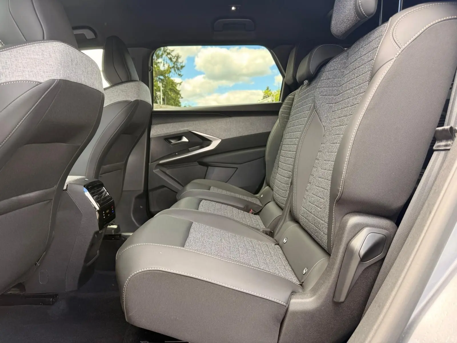 Vue latérale droite de la banquette arrière en tissu gris et cuir noir du Peugeot 5008 Hybrid 2025 avec fenêtre et ciel visible.