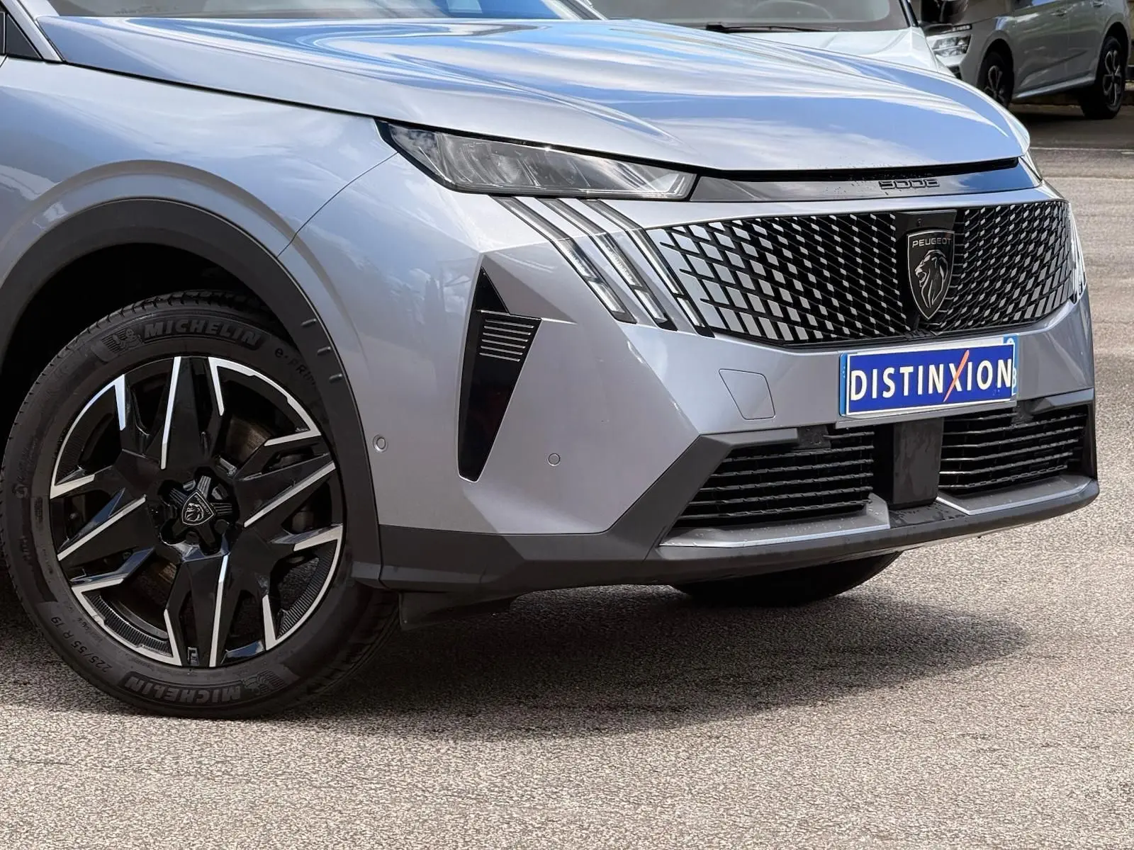 Vue avant droite du Peugeot 5008 gris Artense 2025, avec calandre noire distinctive et jante alliage bicolore.