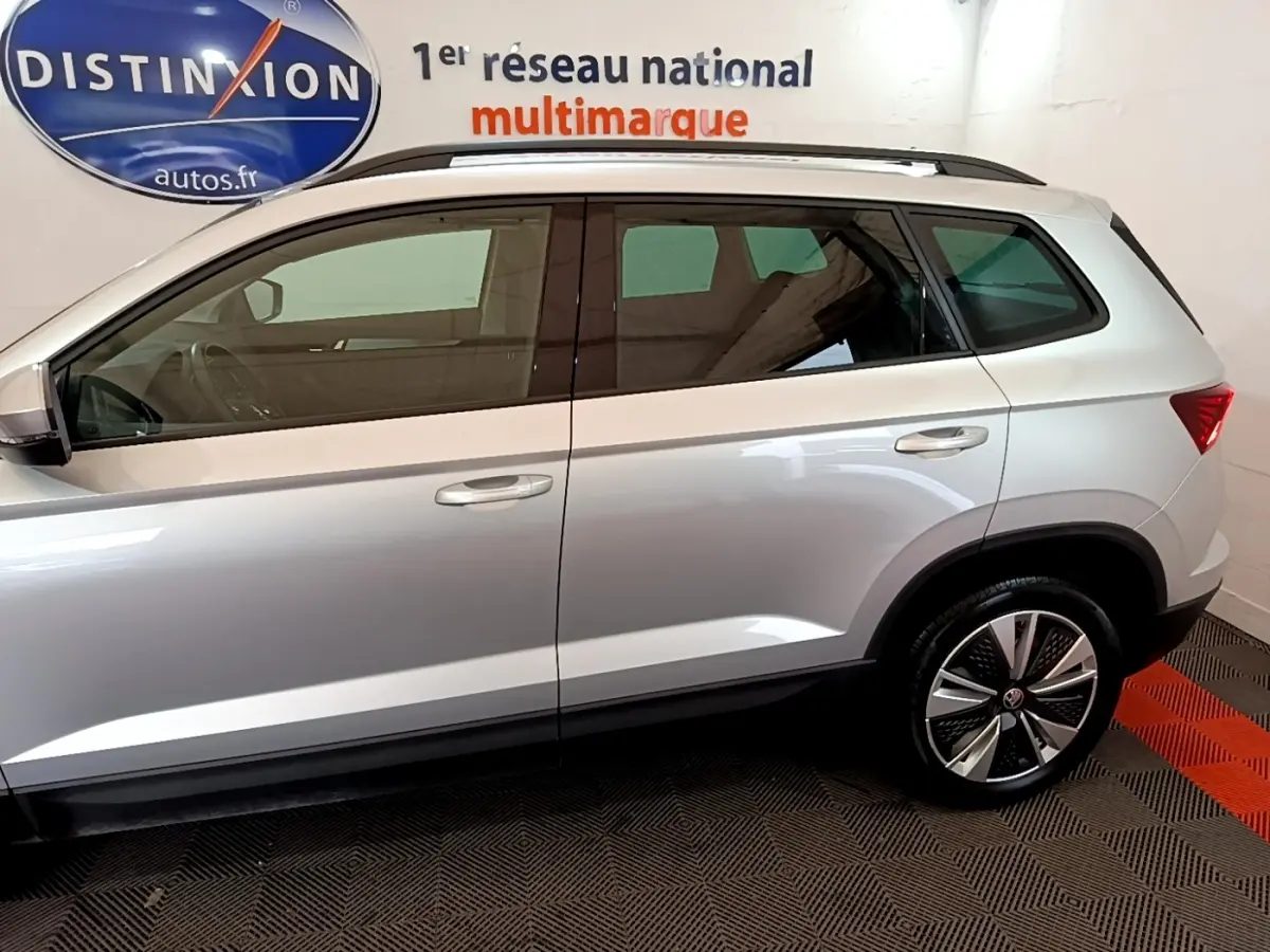 Profil droit du ŠKODA KAROQ gris clair 2022 avec jantes alliage et vitres teintées en intérieur showroom.