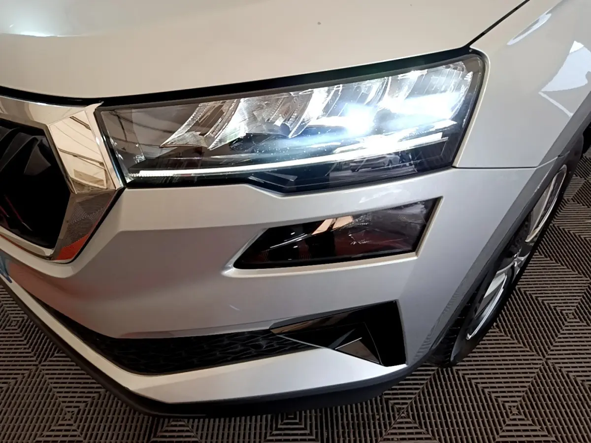 Gros plan sur l'avant droit gris clair du Skoda Karoq 2022 avec phares LED allumés et calandre chromée.