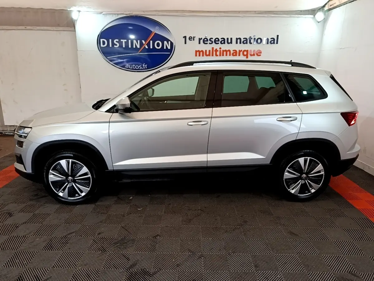 Vue latérale droite d'un Skoda Karoq gris clair 2022, avec jantes alliage et toit noir, en intérieur showroom.