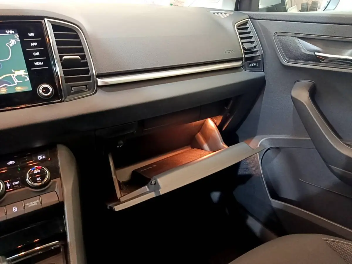 Vue intérieure côté passager du tableau de bord gris foncé d’un Skoda Karoq 2022 avec boîte à gants ouverte et éclairage intérieur.