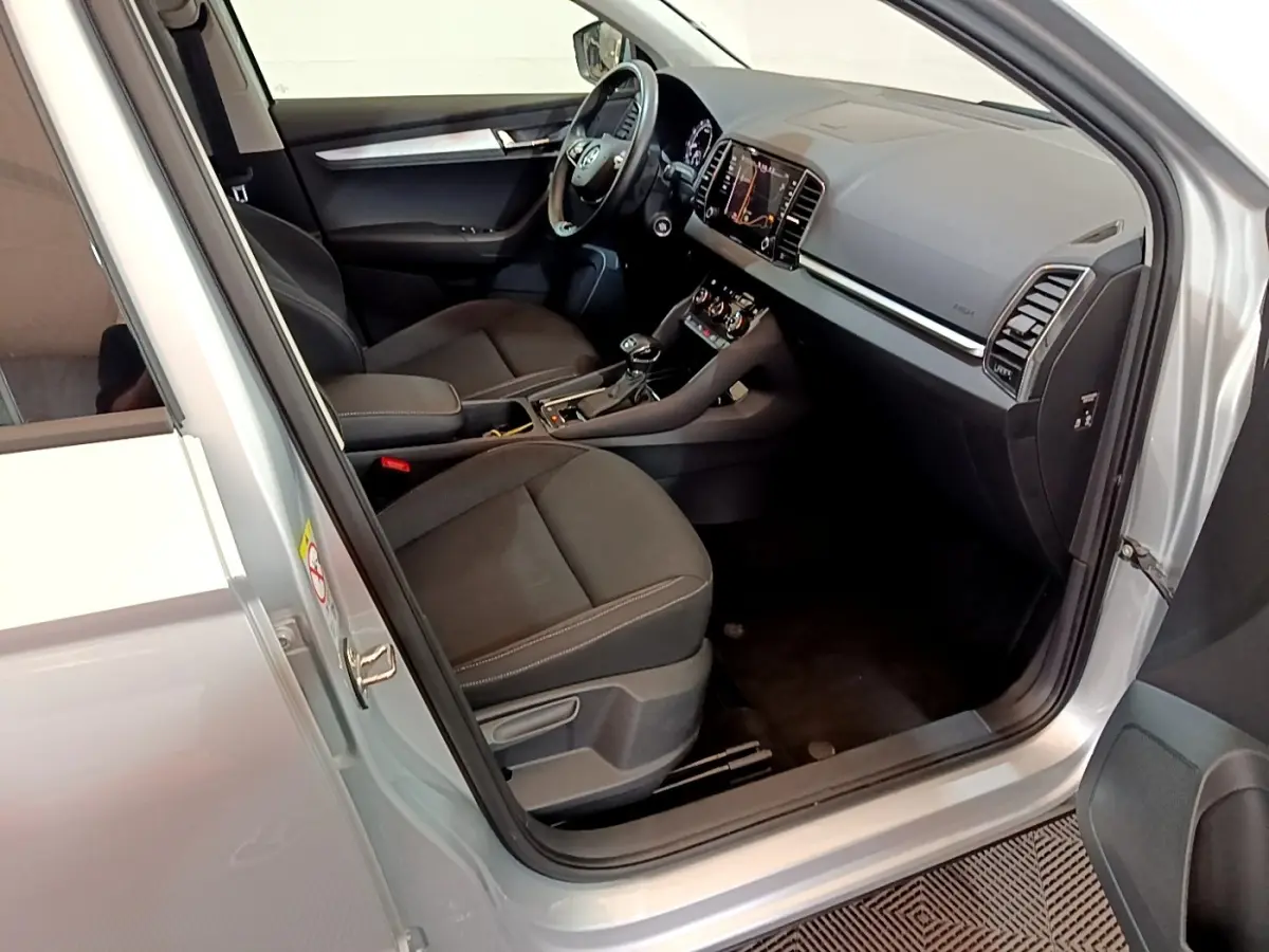 Vue intérieure côté conducteur d'un Skoda Karoq gris clair, montrant sièges noirs et tableau de bord avec écran tactile.