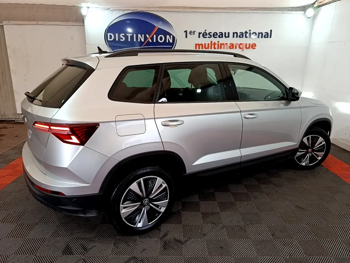 Vue 3/4 arrière droite d’un Skoda Karoq gris clair 2022 avec feux arrière LED et jantes alliage distinctives.