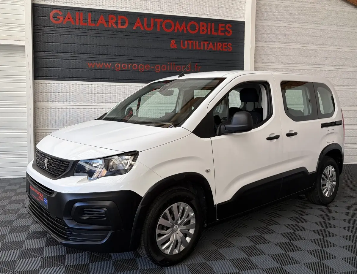 Vue 3/4 avant droit d’un Peugeot Rifter blanc 2021 avec pare-chocs noirs et jantes acier.