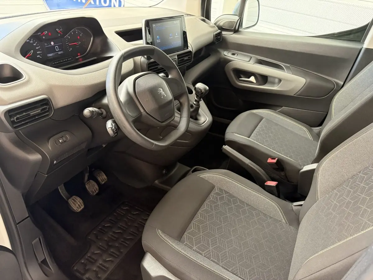 Vue intérieure côté conducteur du Peugeot Rifter blanc 2021, montrant le volant, tableau de bord et sièges tissu gris.
