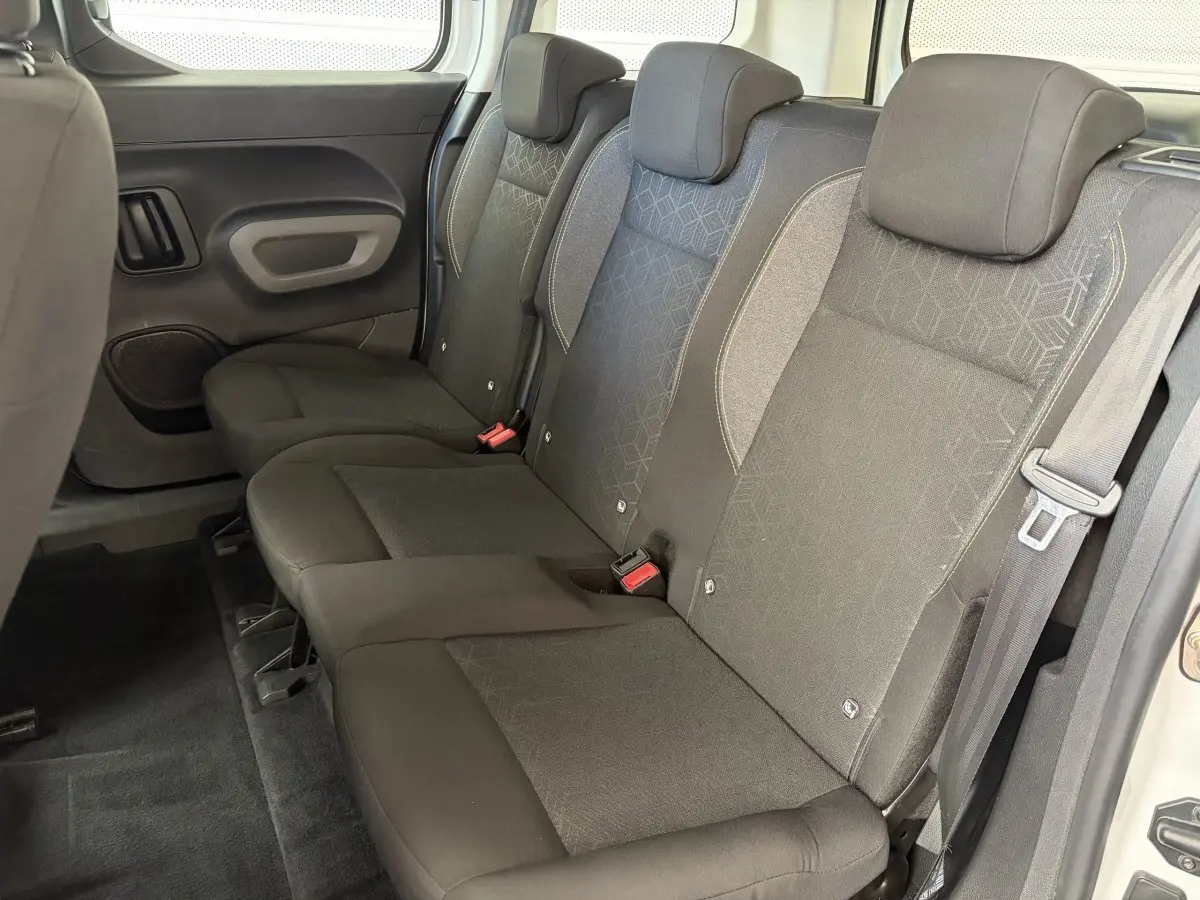 Vue latérale droite sur la banquette arrière noire du Peugeot Rifter blanc, montrant trois sièges avec appuie-têtes.