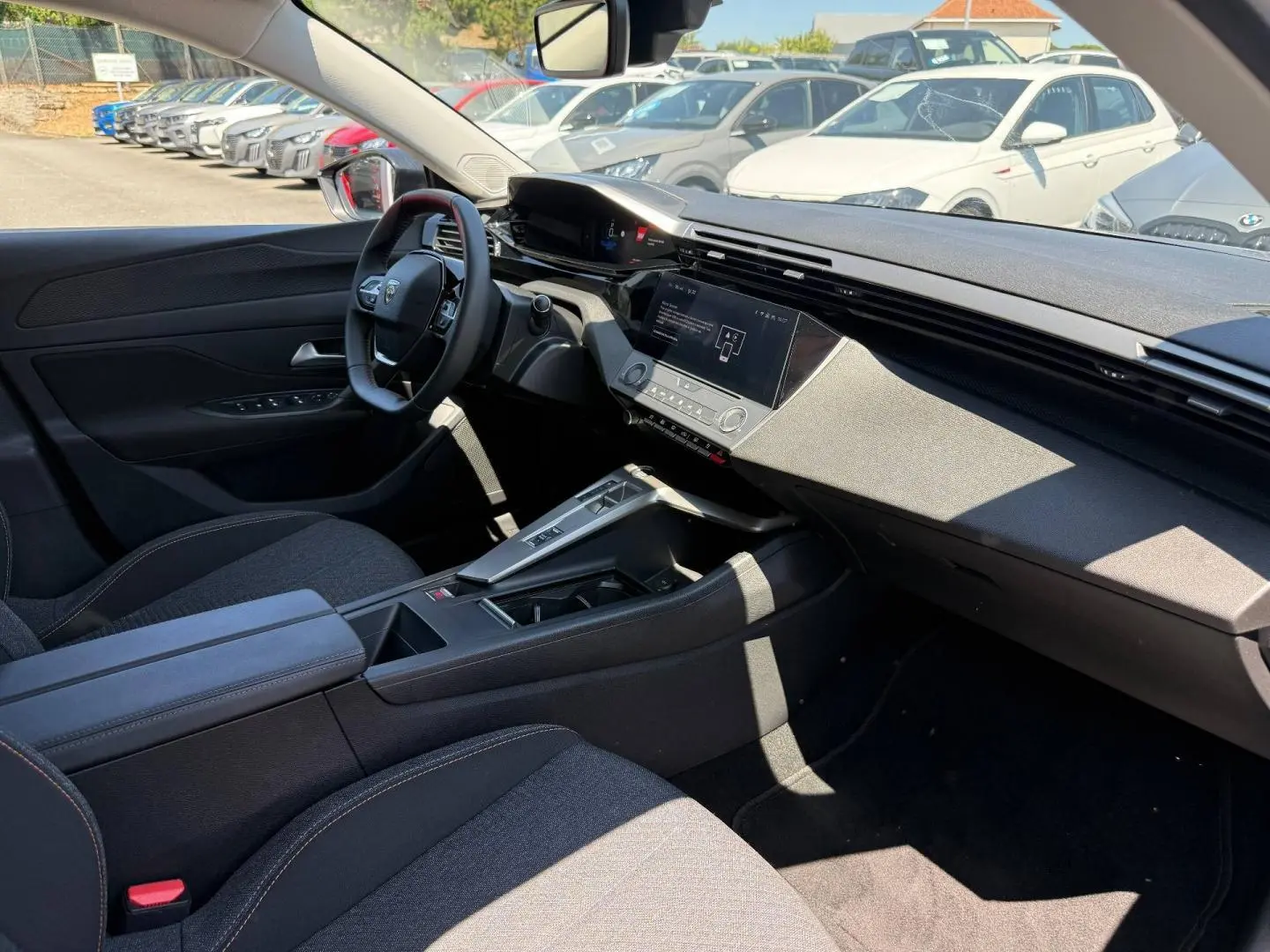 Intérieur de la Peugeot e-308 2025 vu côté conducteur, tableau de bord moderne avec écran tactile et sièges tissu gris.