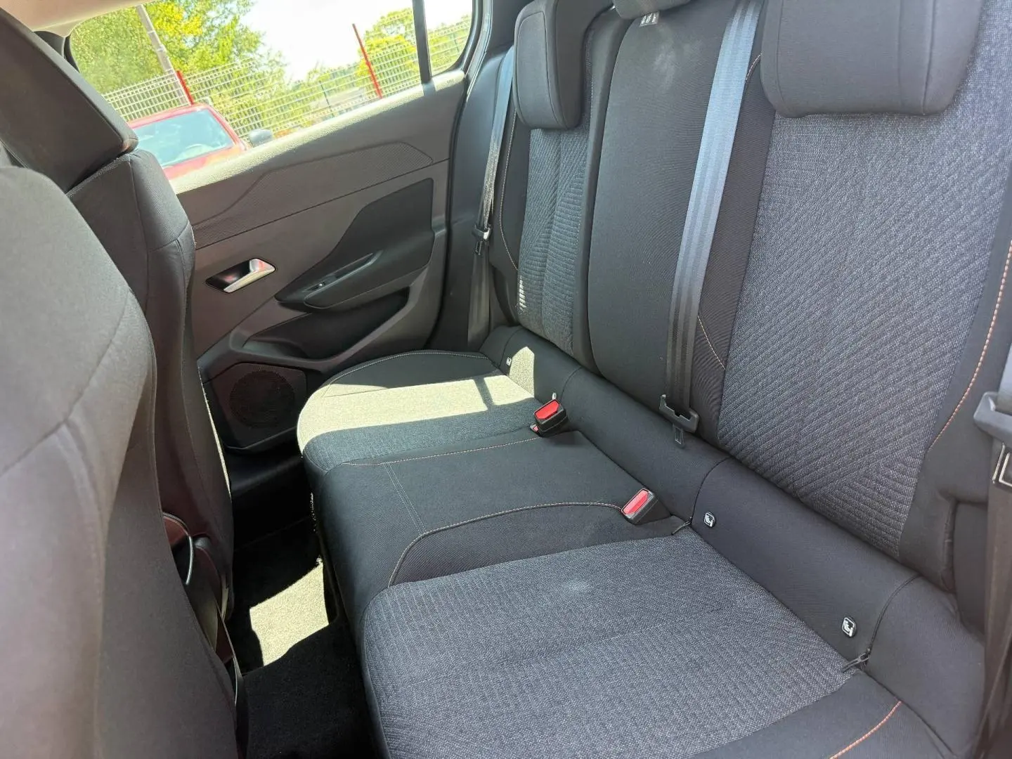 Vue intérieure côté arrière gauche montrant la banquette tissu noir et gris avec surpiqûres orange de la Peugeot e-308 2025.
