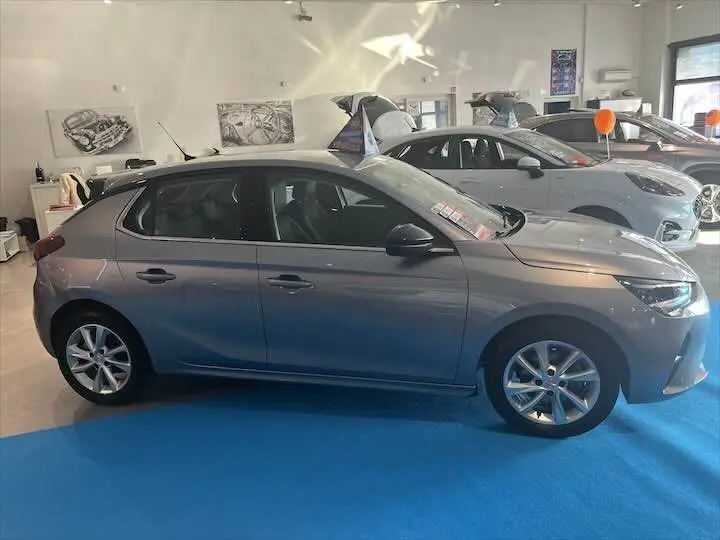 Profil côté gauche d'une Opel Corsa gris métal 2021 exposée en showroom avec jantes alliage et vitres teintées.