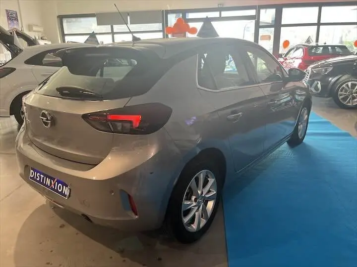 Opel Corsa gris métal vue 3/4 arrière droit en intérieur, avec feux arrière allumés et jantes alliage.
