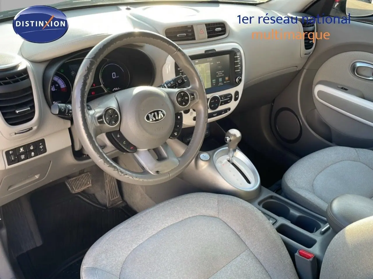 Vue intérieure avant de la Kia Soul EV 2016, montrant le volant, la console centrale avec écran tactile et sièges tissu gris clair.