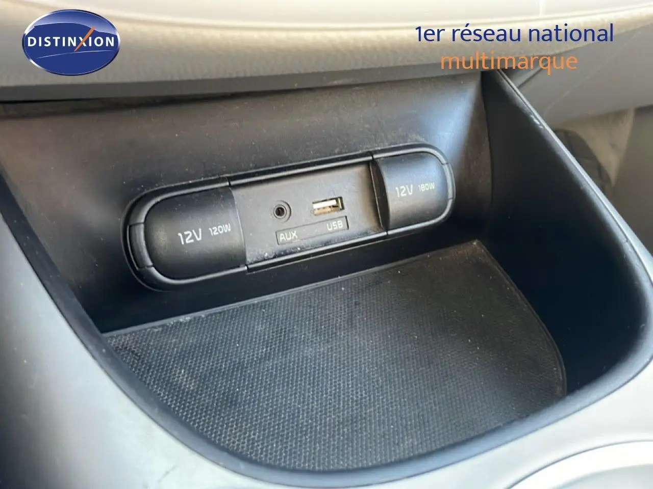 Gros plan sur la console centrale du Kia Soul EV 2016 montrant les prises 12V, USB et AUX dans un intérieur noir.