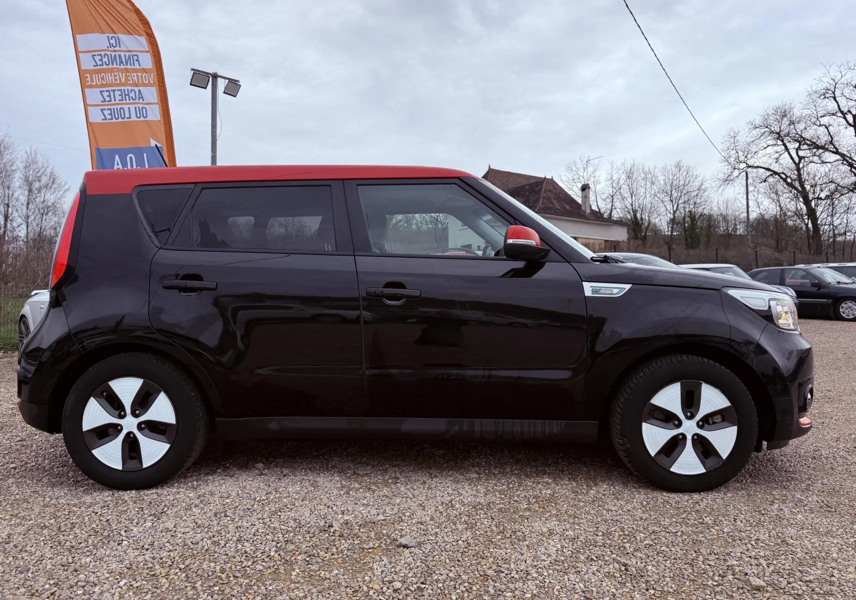 Vue arrière d'une KIA SOUL EV électrique noire avec toit rouge, mettant en valeur ses feux verticaux et son design compact.