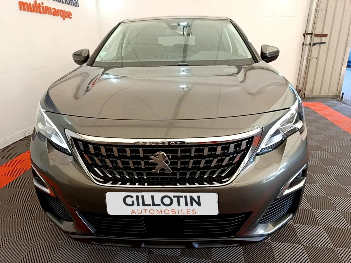 Vue avant d'un Peugeot 3008 gris foncé avec calandre chromée et phares LED, en intérieur showroom.