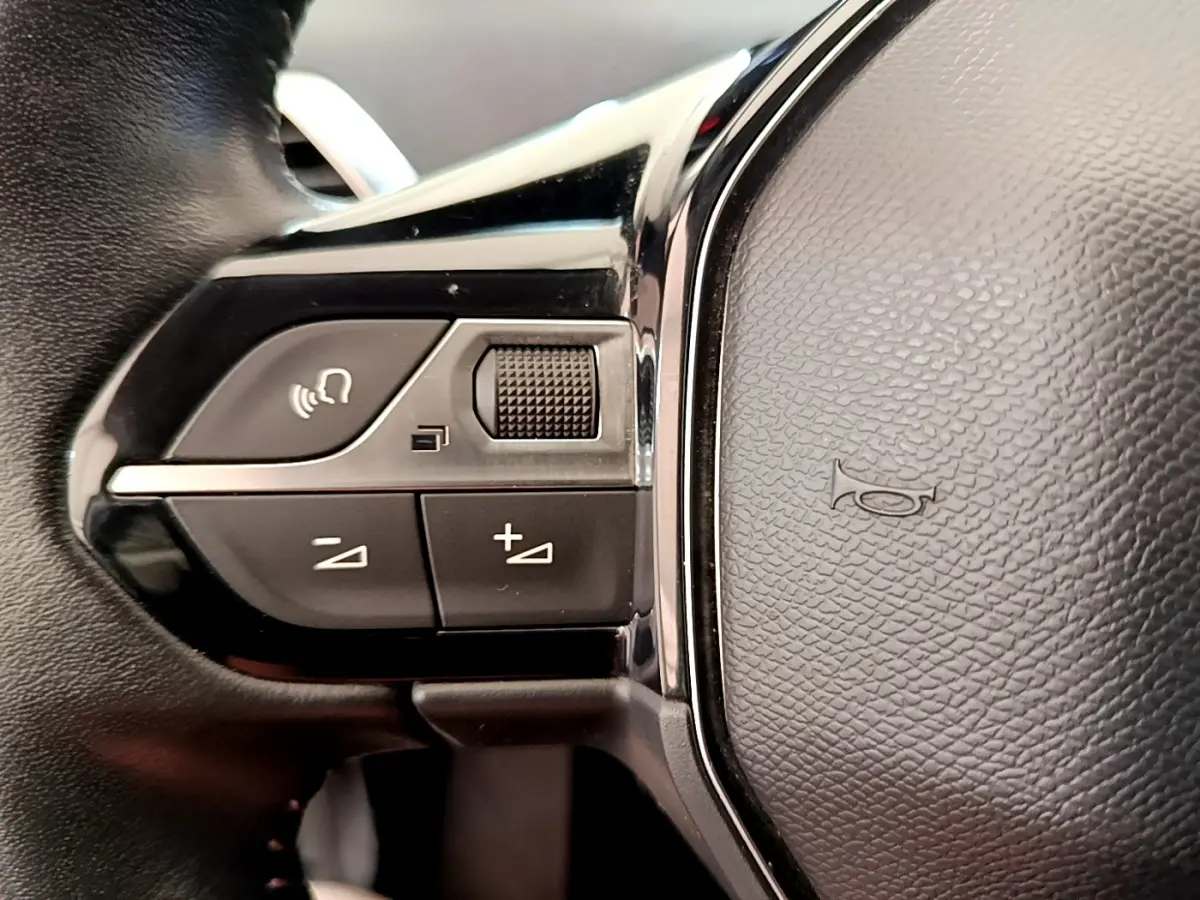 Gros plan sur les commandes gauche du volant cuir noir du Peugeot 3008 gris foncé, avec boutons de volume et commande vocale.