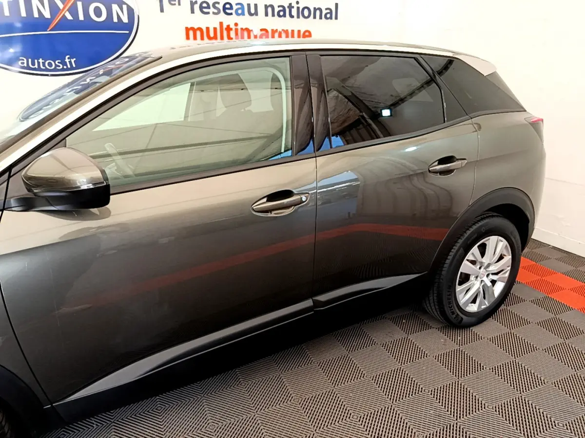 Vue latérale côté gauche d'un Peugeot 3008 gris foncé garé en intérieur avec jantes argentées visibles.