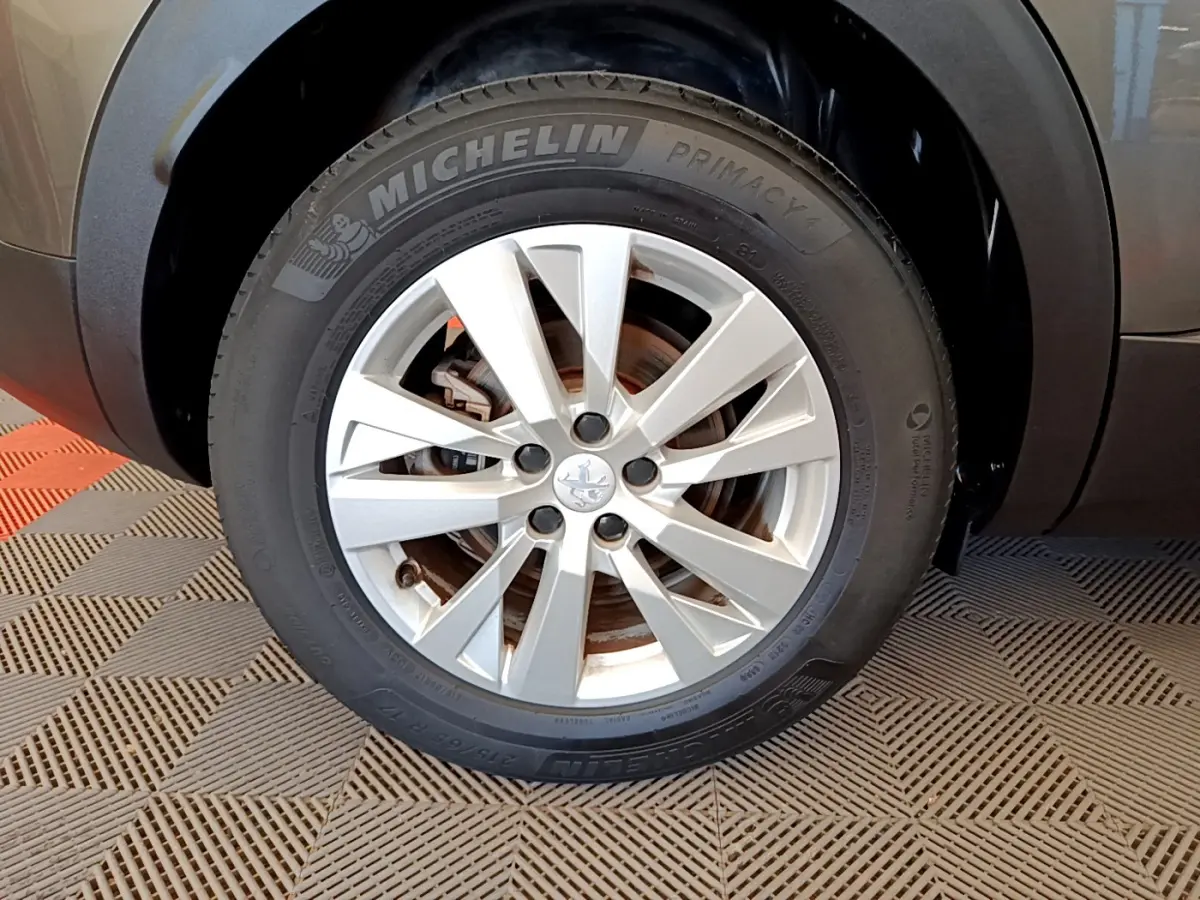 Gros plan sur la roue avant droite d'un Peugeot 3008 gris foncé, avec jante alliage et pneu Michelin Primacy 4.