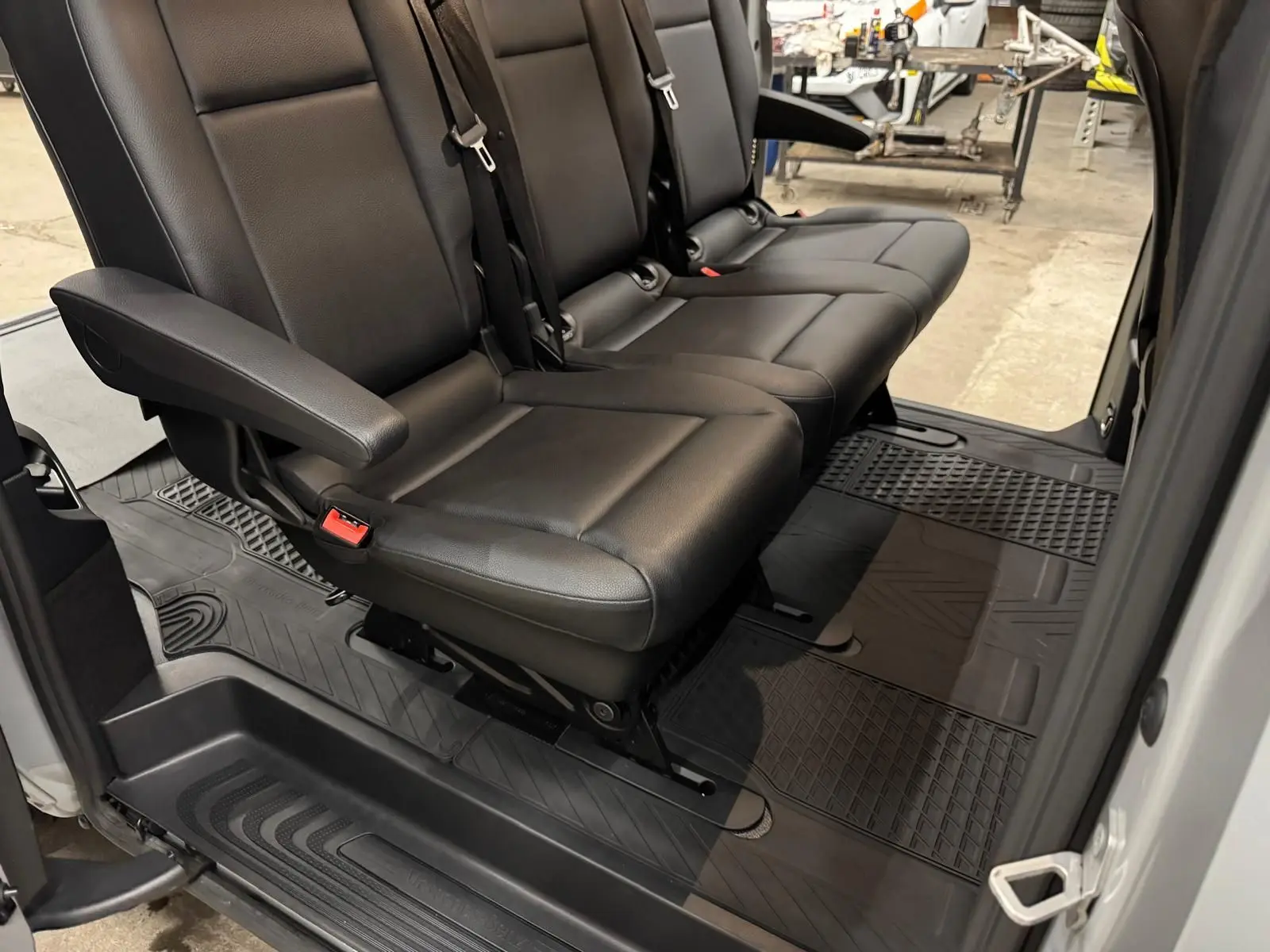 Vue intérieure côté droit sur la banquette noire 3 places en cuir avec tapis de sol caoutchouc dans un Mercedes Vito Mixto gris.