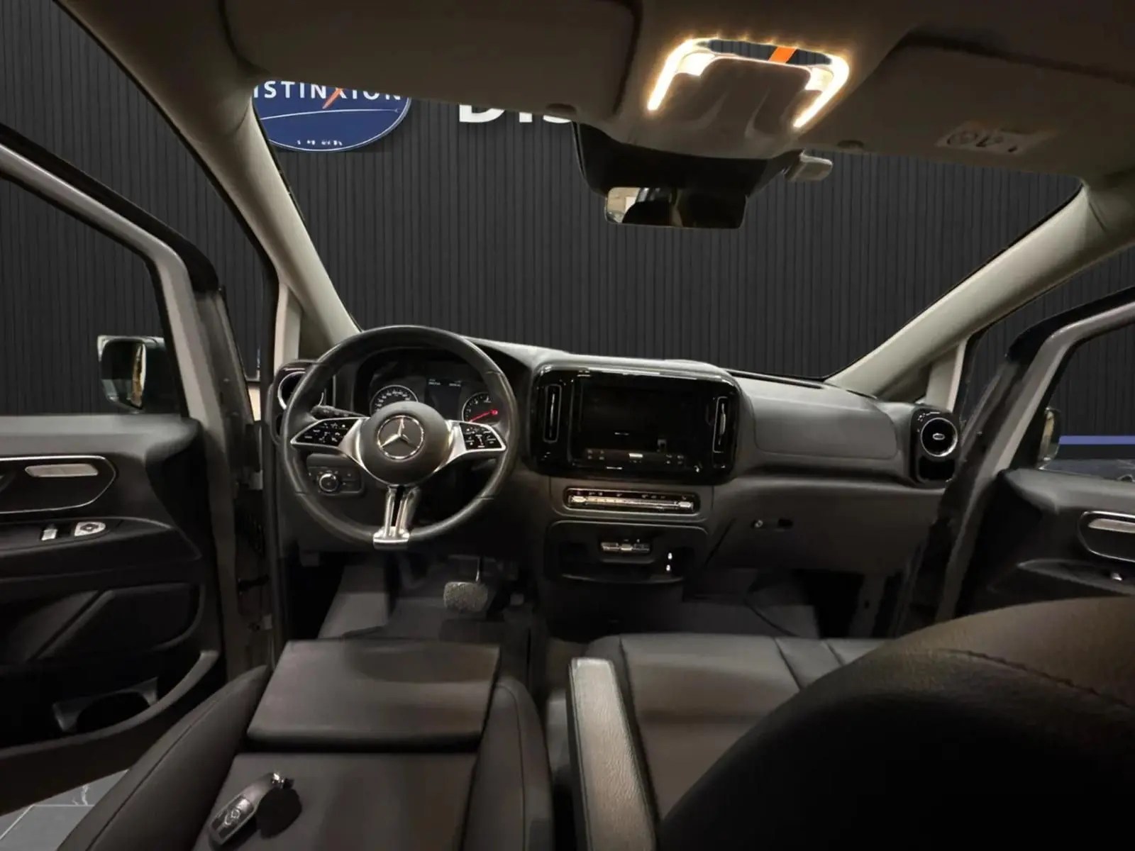 Vue intérieure avant du Mercedes Vito Mixto 2025, tableau de bord noir avec volant multifonction et écran central éteint.