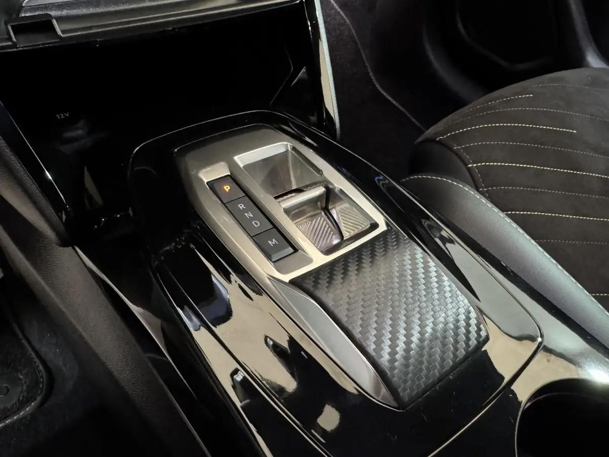 Gros plan sur la console centrale noire brillante avec sélecteur de boîte auto et finition carbone dans une Peugeot 208 Hybrid 136 eDCS6 GT.